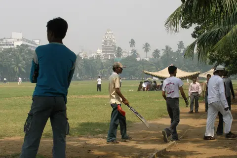 A game underway on the Oval Maidan in Mumbai, city buildings behind the trees